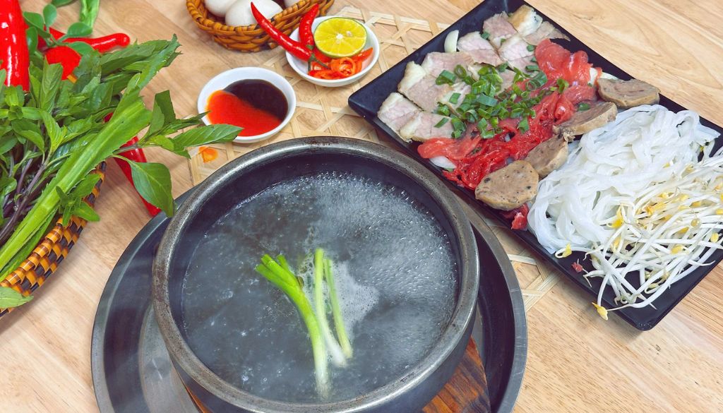 A delicious serving of pho in a stone bowl with fresh beef and herbs